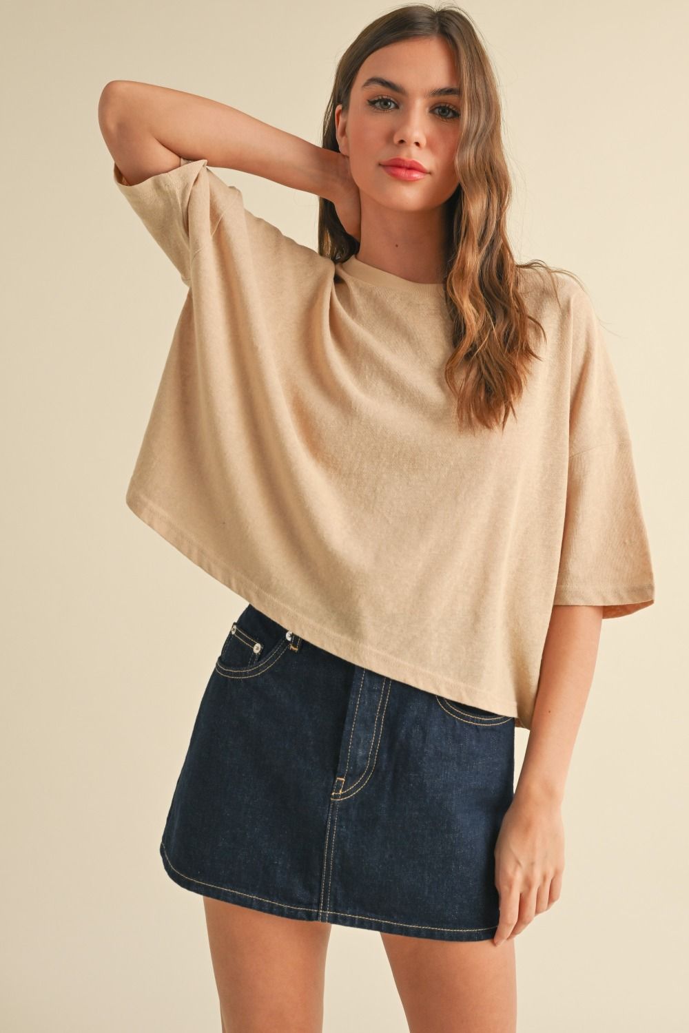 Woman wearing a beige oversized t-shirt and denim skirt on a beige background