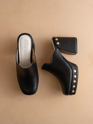 Black leather clog shoe with studded details on a beige background