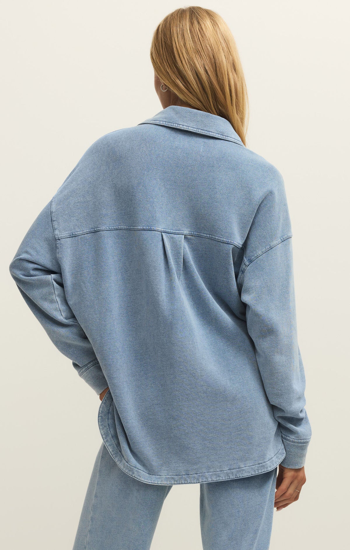 Person wearing a light blue denim jacket on a plain background