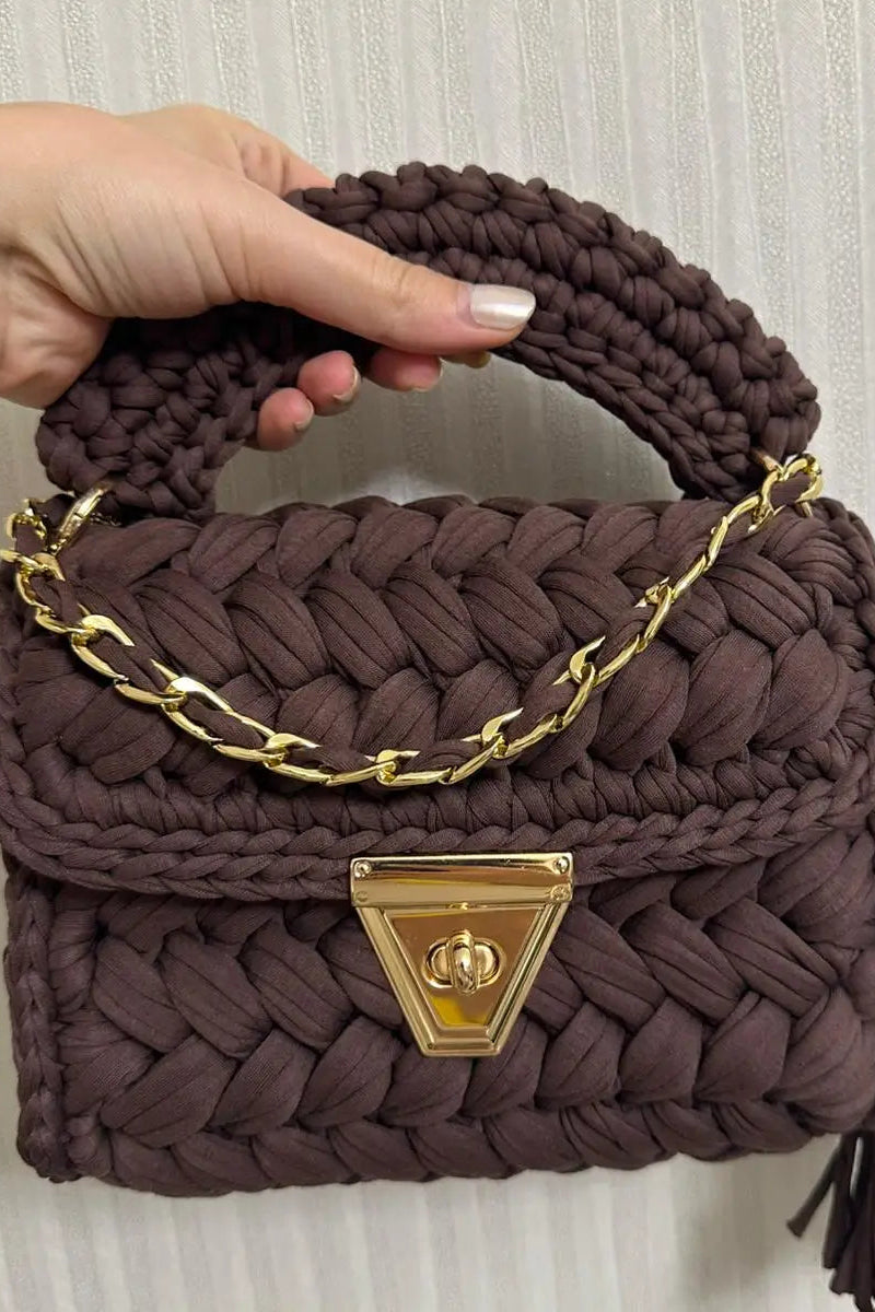 Brown woven handbag with gold chain handle and clasp held by a hand.