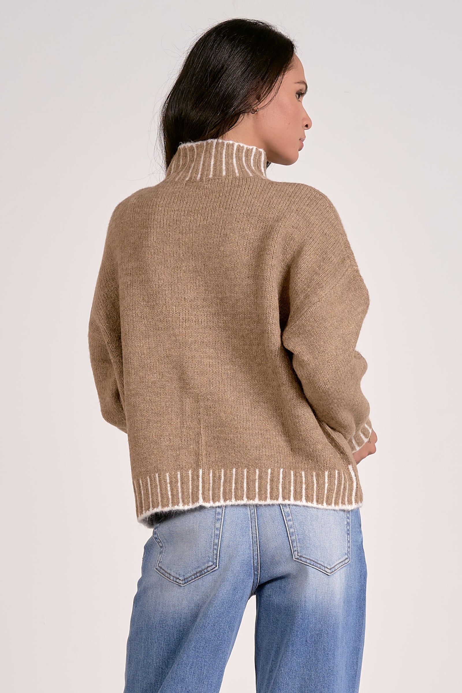 Woman wearing a beige sweater with white trim on a plain background