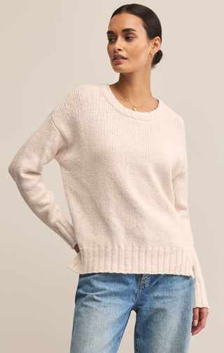 Woman wearing a light pink sweater and blue jeans against a neutral background