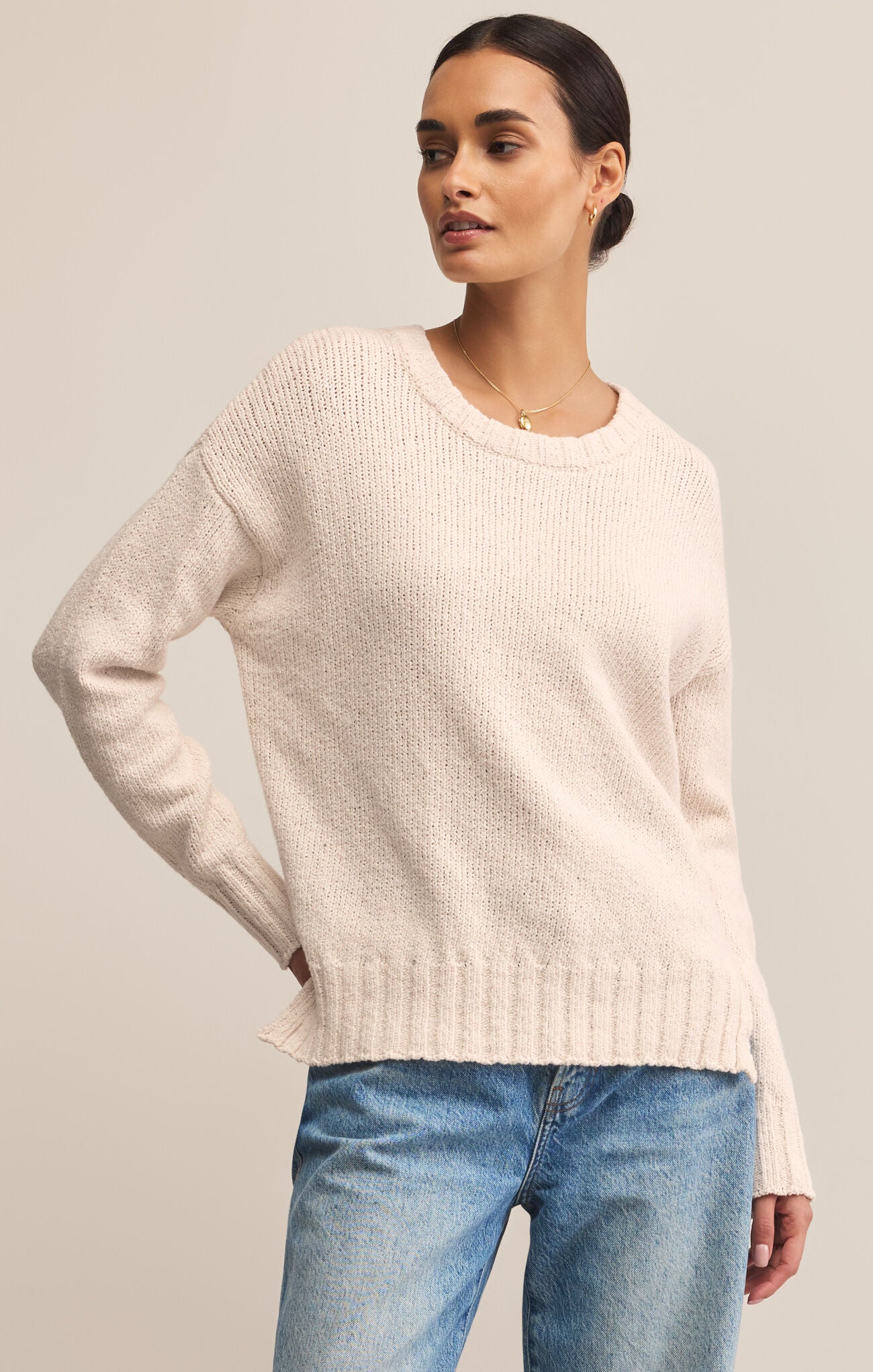 Woman wearing a light pink sweater and blue jeans against a neutral background