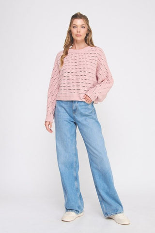 Woman wearing a pink patterned sweater and blue jeans on a white background