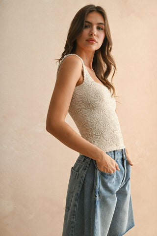 Woman wearing a white lace tank top and denim shorts against a beige background