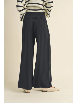 Person wearing black wide-leg pants and a striped sweater on a beige background