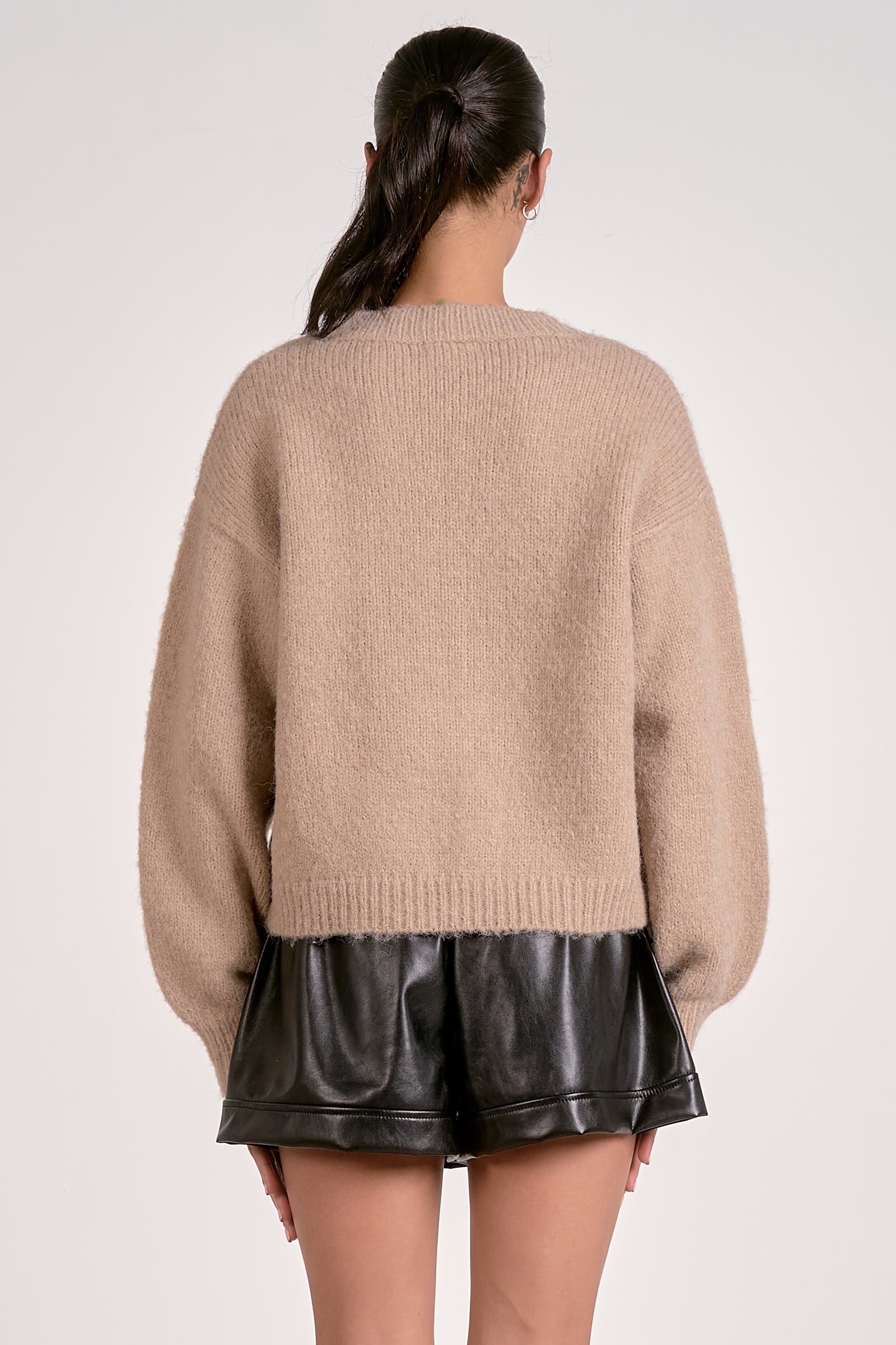 Woman wearing a beige cardigan and black leather shorts on a white background