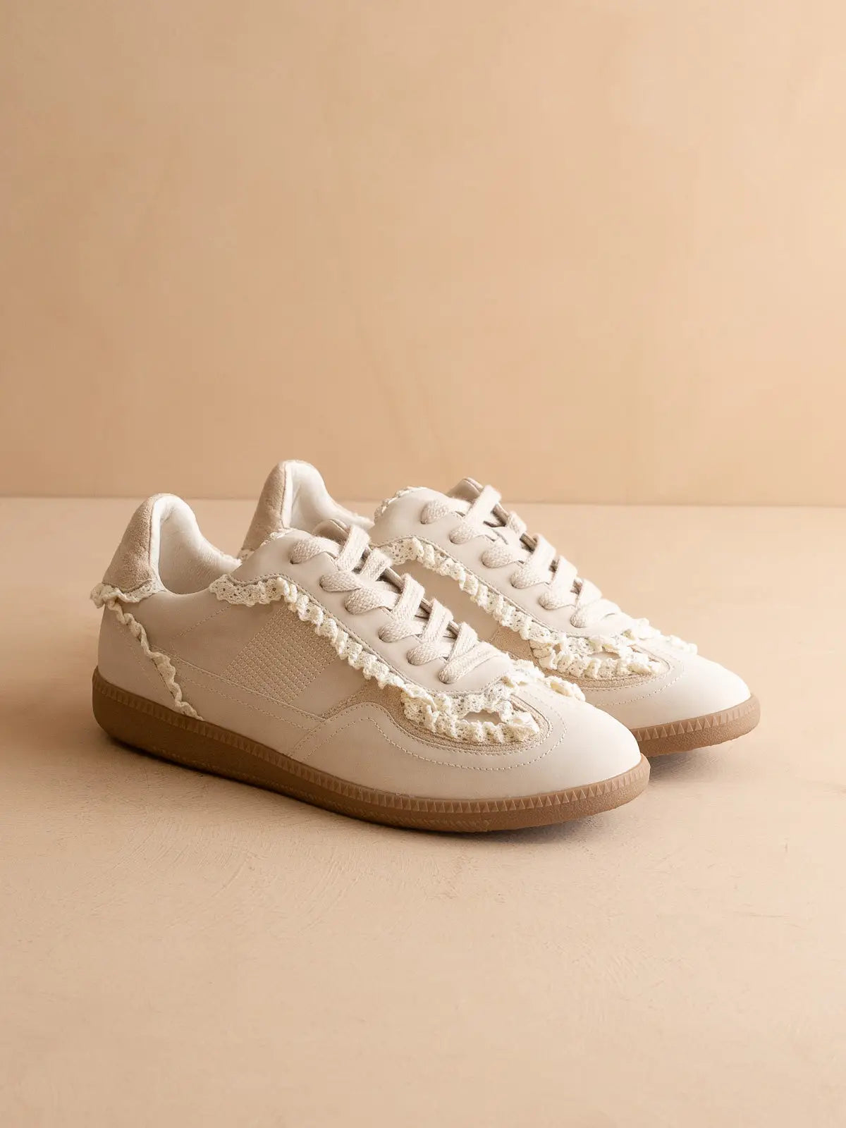 White sneakers with lace details on a beige background