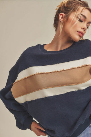 Woman wearing a navy sweater with color-blocked design on a neutral background