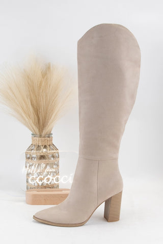 Beige knee-high boot on a white background with a decorative vase.