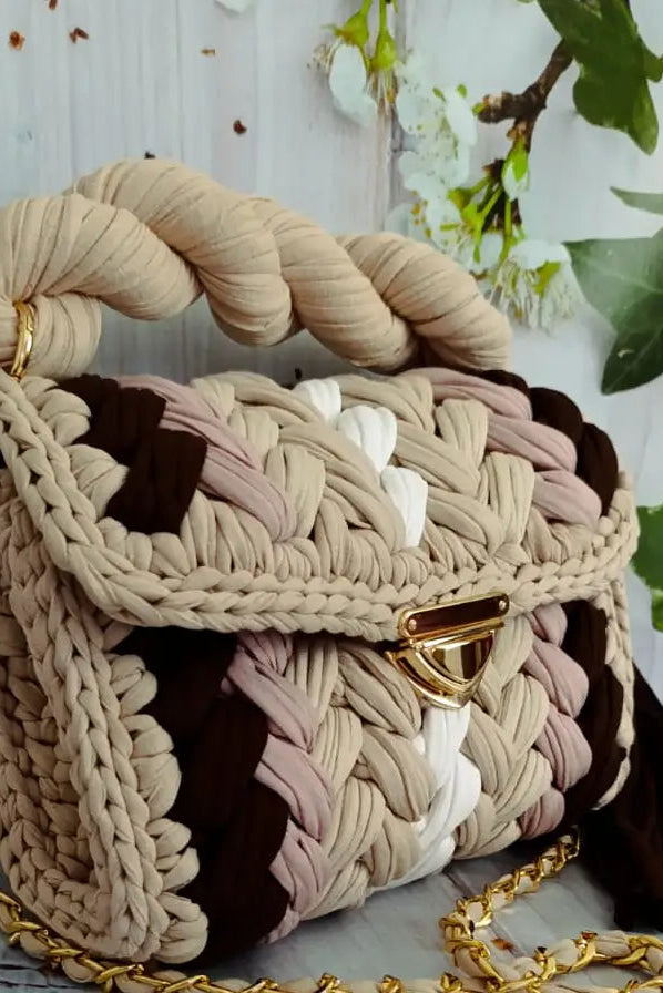Woven handbag with braided handle and gold accents on a light background