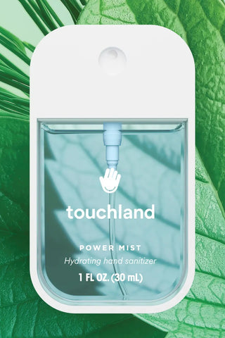Touchland power mist hand sanitizer packaging on a green leaf background