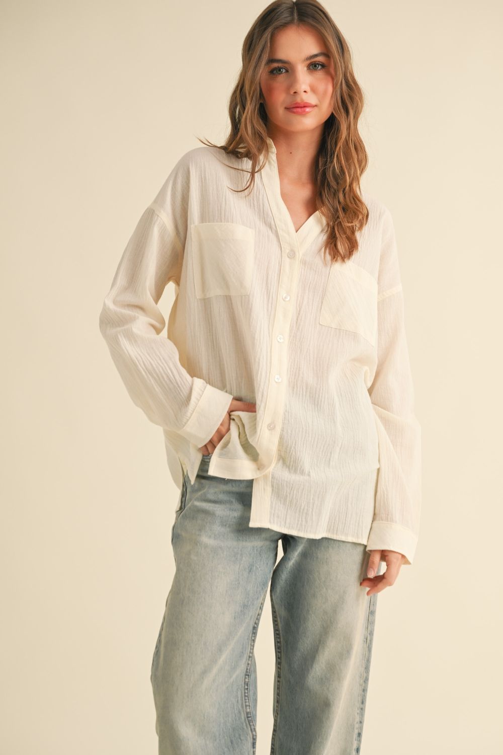 Woman wearing a white button-up shirt and light blue jeans against a beige background