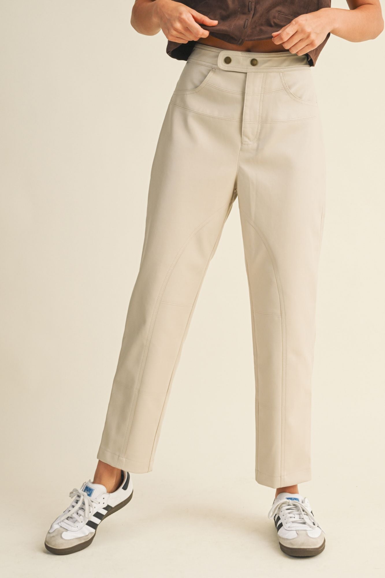 Person wearing beige pants and Adidas sneakers on a plain background