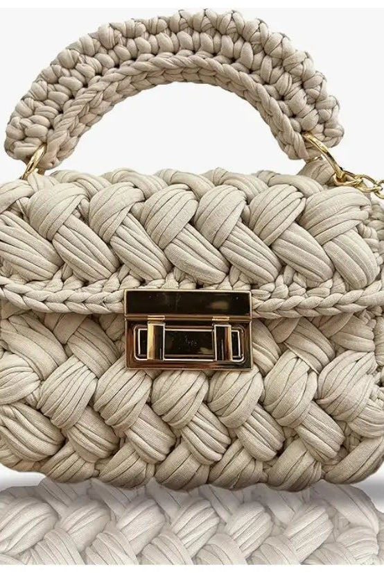 Beige woven handbag with a gold clasp on a reflective surface