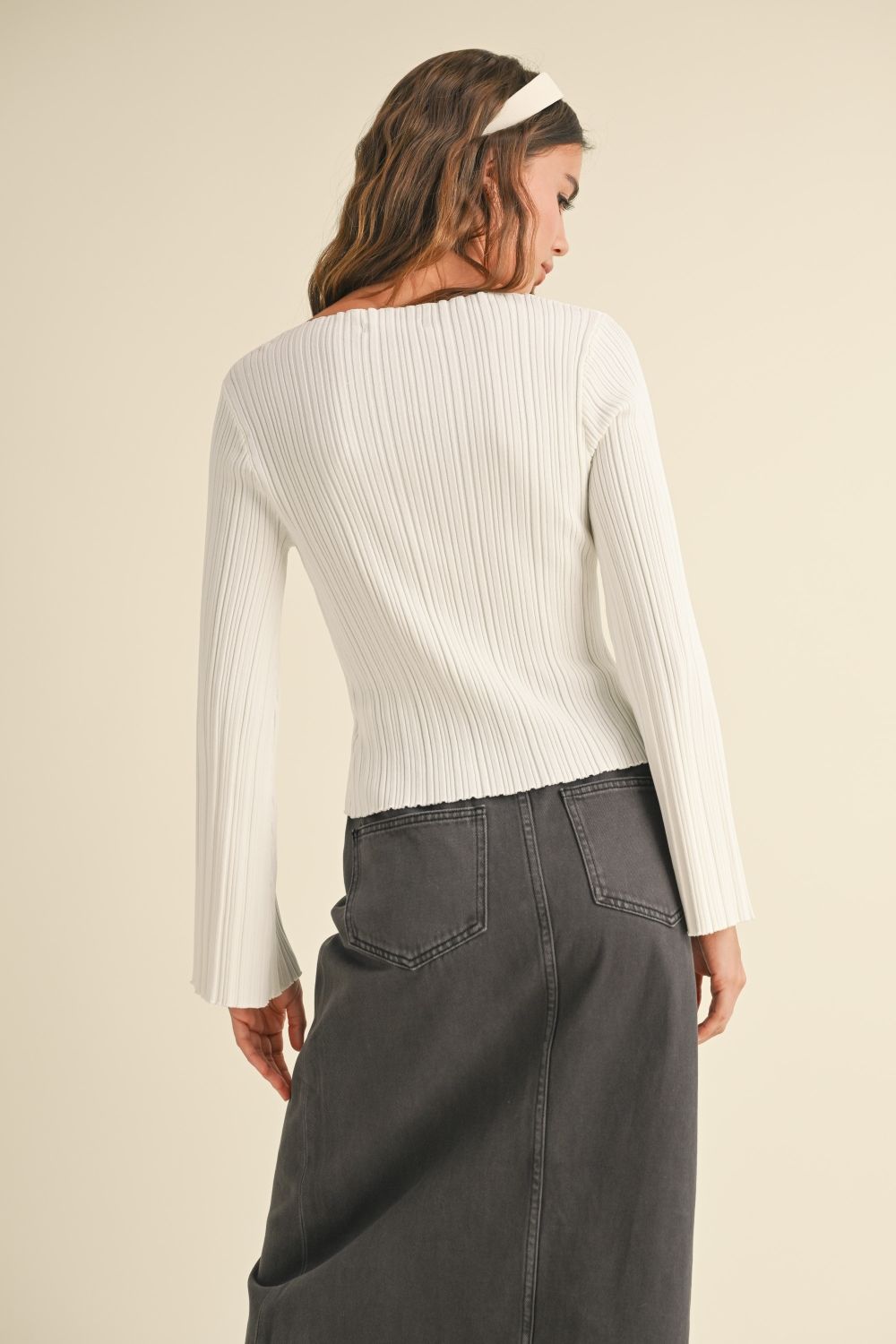 Woman wearing a white ribbed sweater and gray pants on a beige background