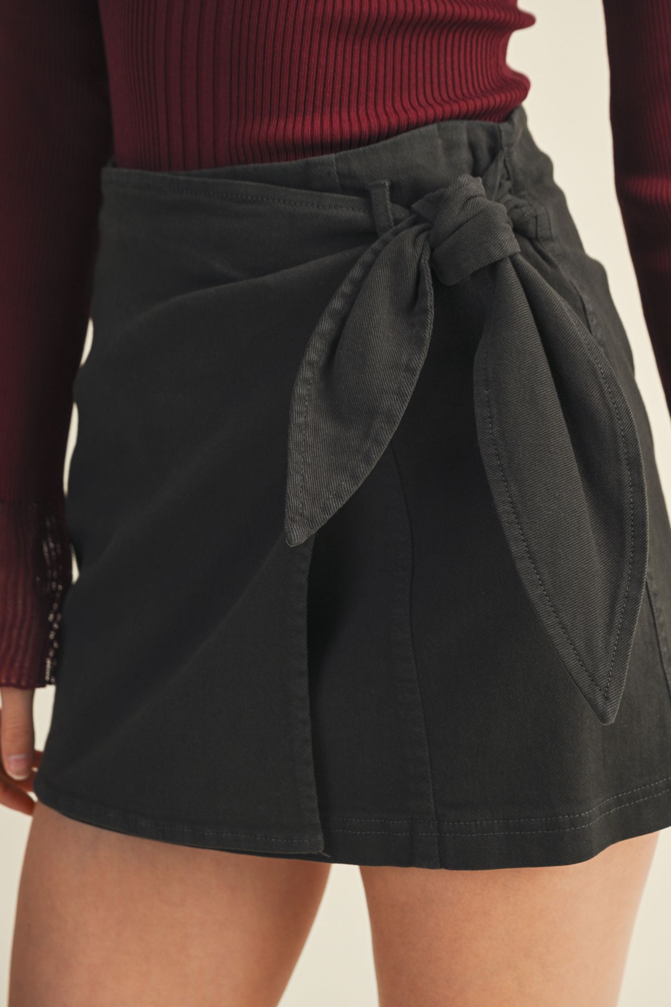 Black skirt with a tie waist worn by a person, against a neutral background
