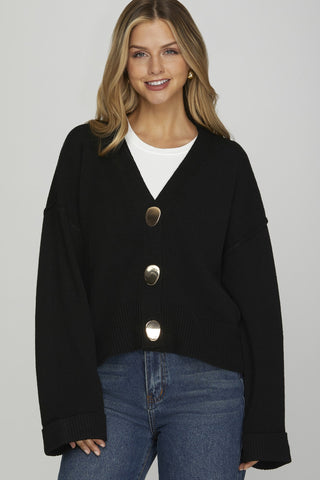 Woman wearing a black cardigan with silver buttons on a gray background