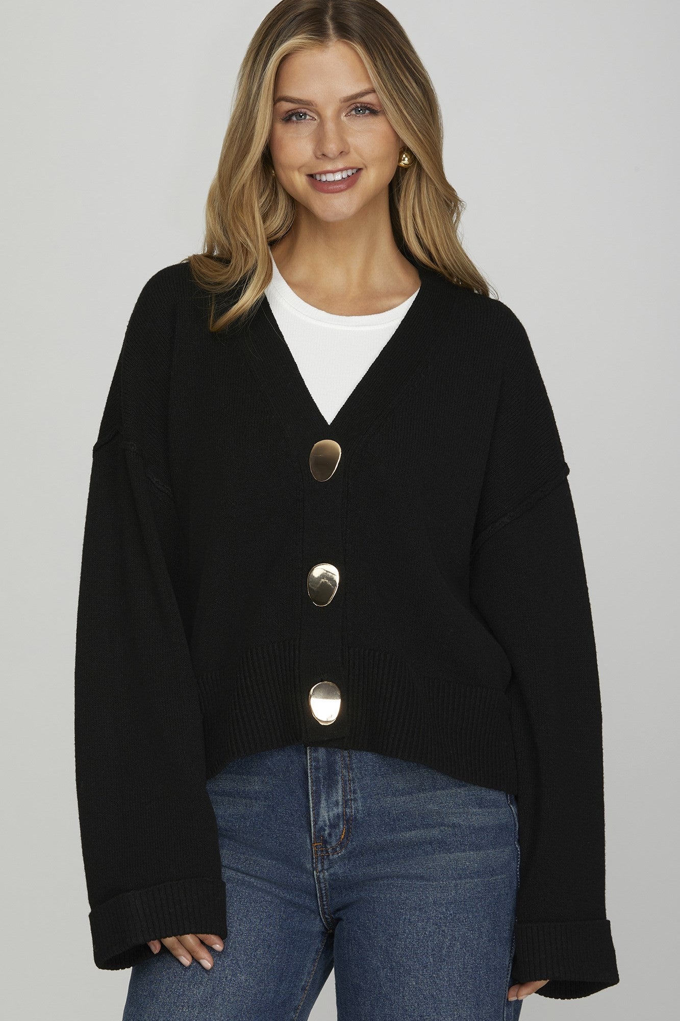 Woman wearing a black cardigan with silver buttons on a gray background