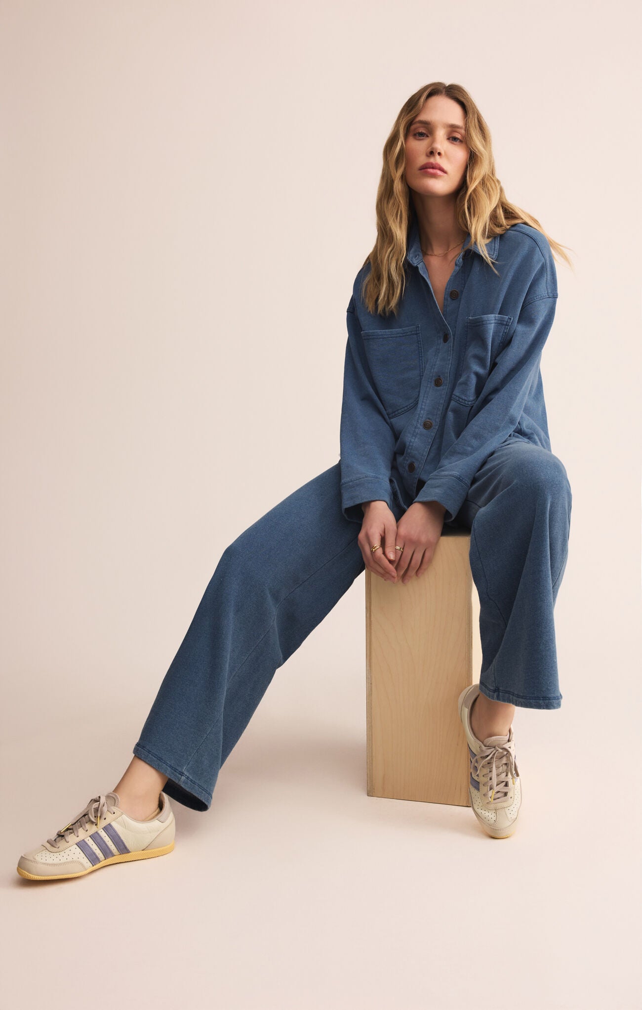 Woman wearing a blue denim outfit sitting on a box against a beige background