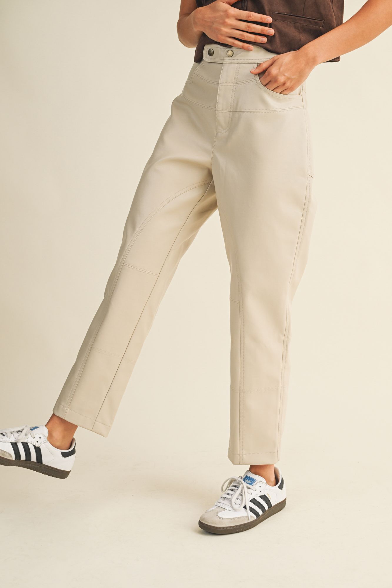 Person wearing beige pants and Adidas sneakers on a plain background