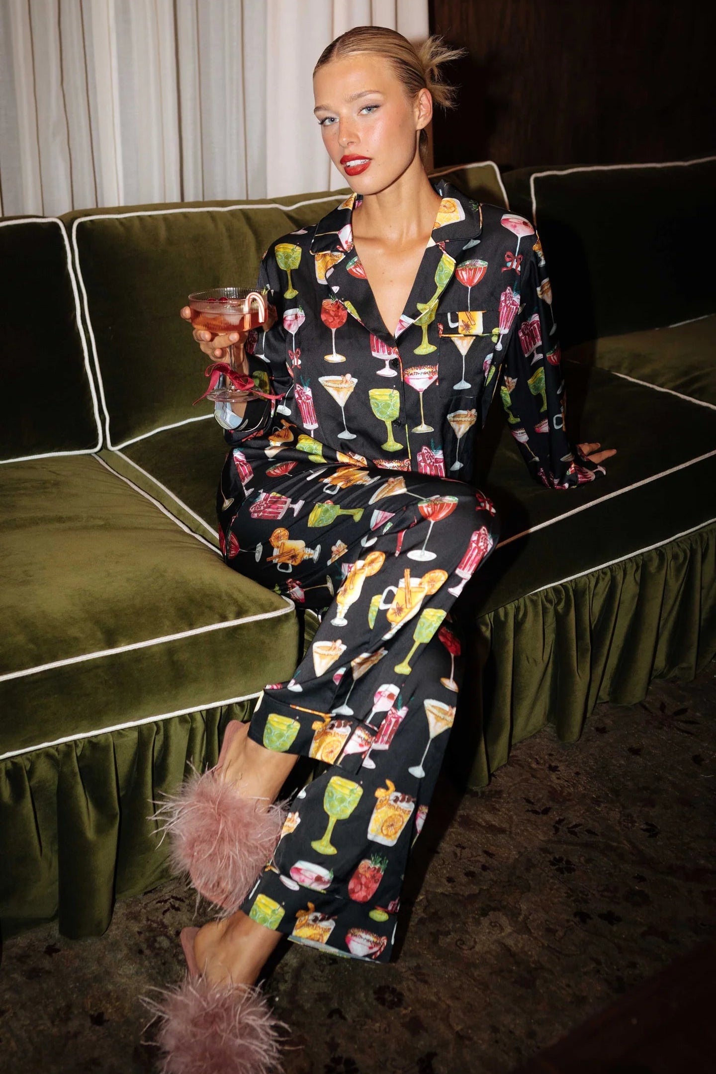 Woman in pajama set with cocktail pattern sitting on a green couch.