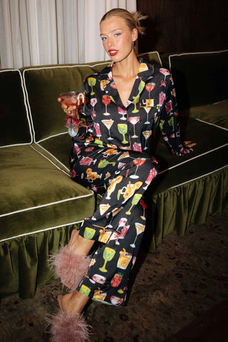 Woman in pajama set with cocktail pattern sitting on a green couch.