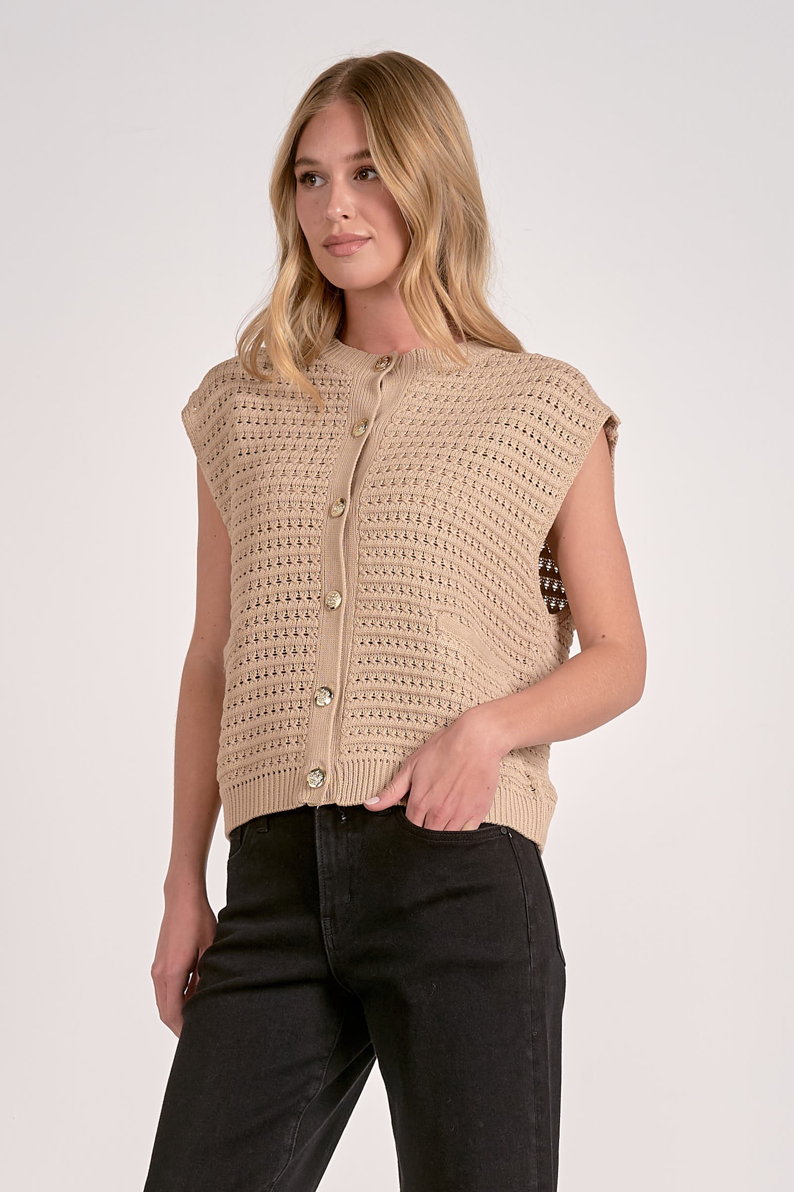 Woman wearing a beige sleeveless knitted top with buttons on a white background
