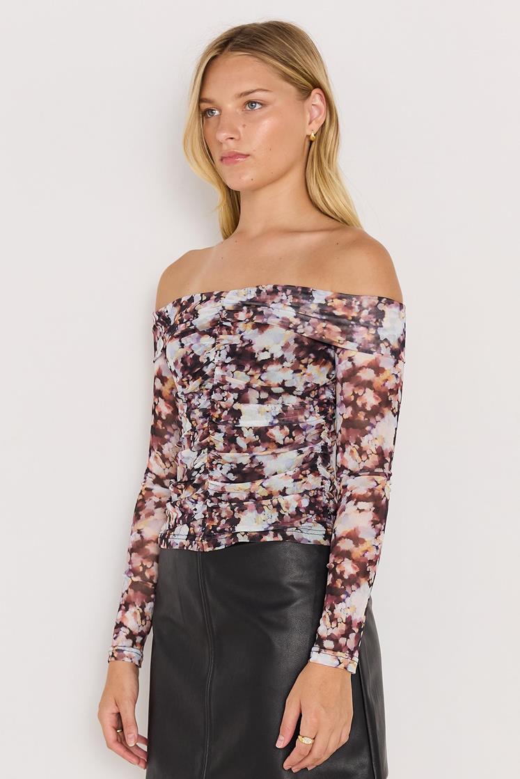 Woman wearing a floral off-shoulder top and black pants against a white background