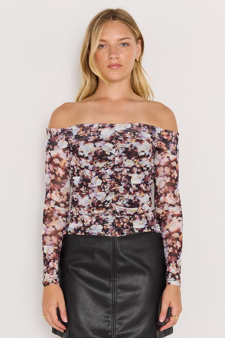 Woman wearing a floral off-shoulder top and black leather skirt on a white background