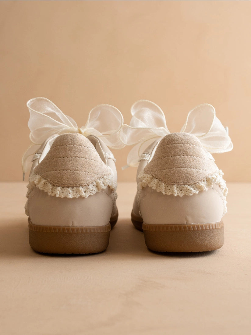 Pair of beige shoes with white bows on a beige background