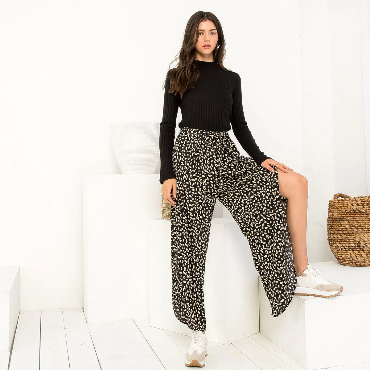 Woman wearing a black top and patterned pants sitting on a white couch.