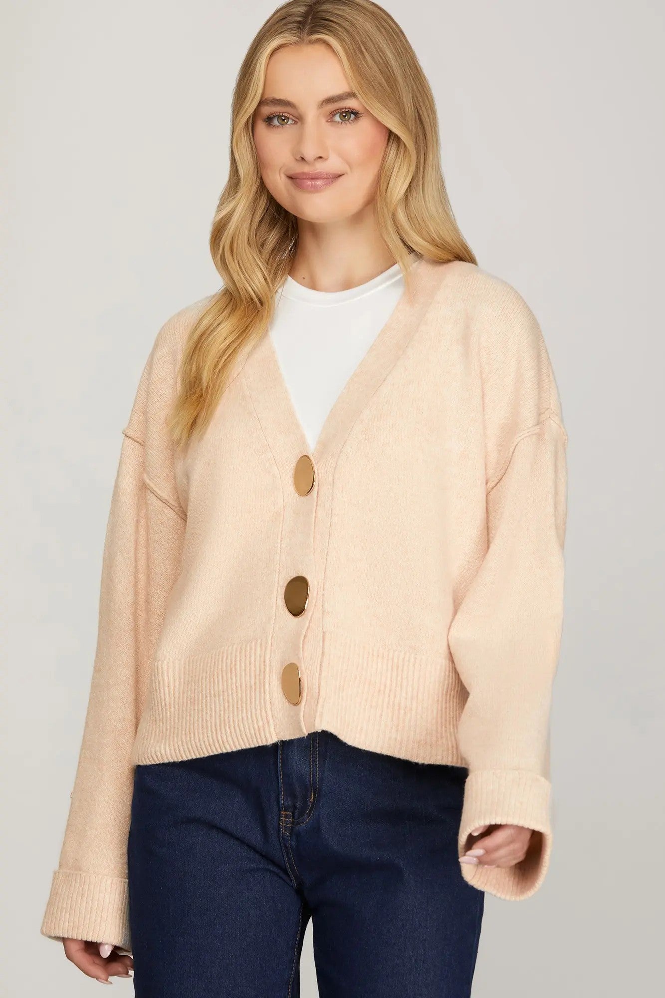 Woman wearing a beige cardigan with brown buttons on a plain background