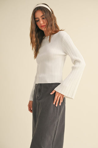 Woman wearing a white ribbed sweater and dark pants on a beige background