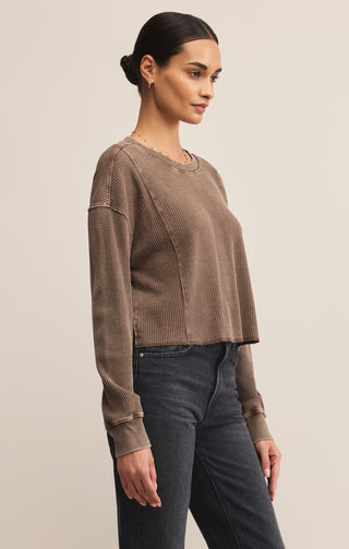 Woman wearing a brown ribbed sweater and dark jeans against a beige background
