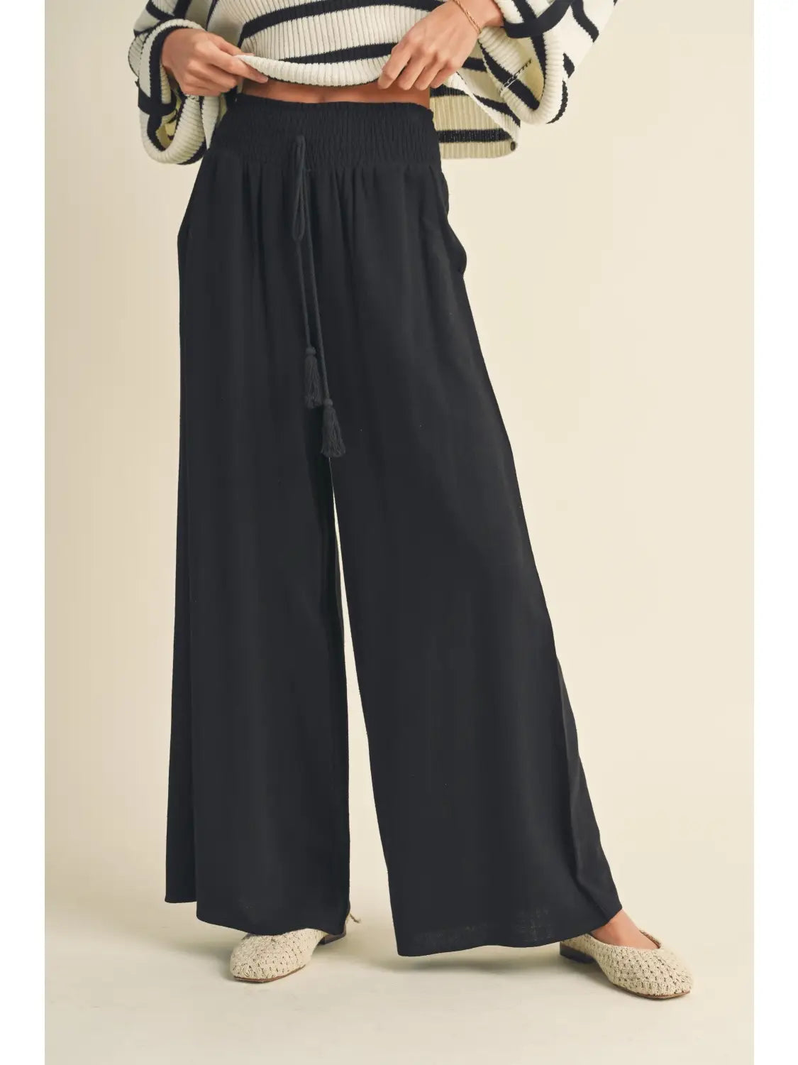 Person wearing black wide-leg pants on a beige background