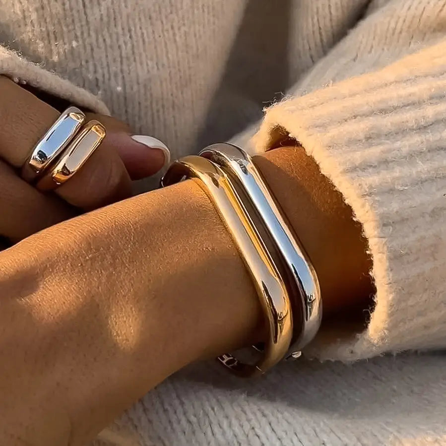 Close-up of a wrist wearing gold bracelets and rings against a neutral background