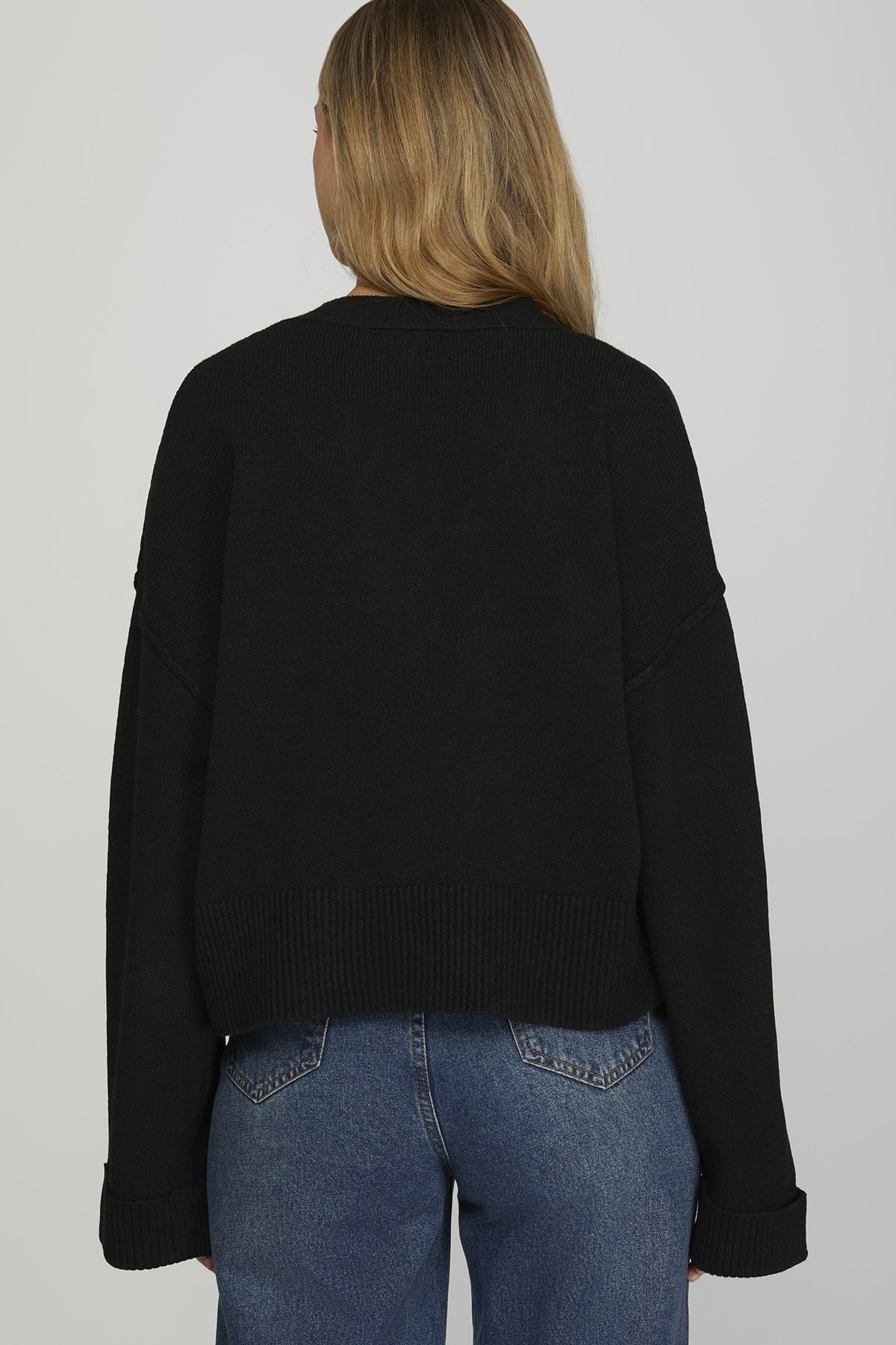 Person wearing a black sweater and blue jeans on a plain background