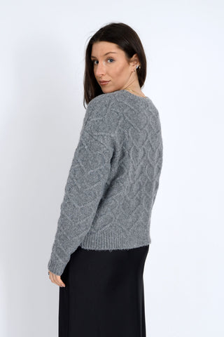 Woman wearing a gray cable knit sweater on a white background