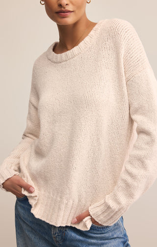 Person wearing a light pink sweater and blue jeans against a neutral background