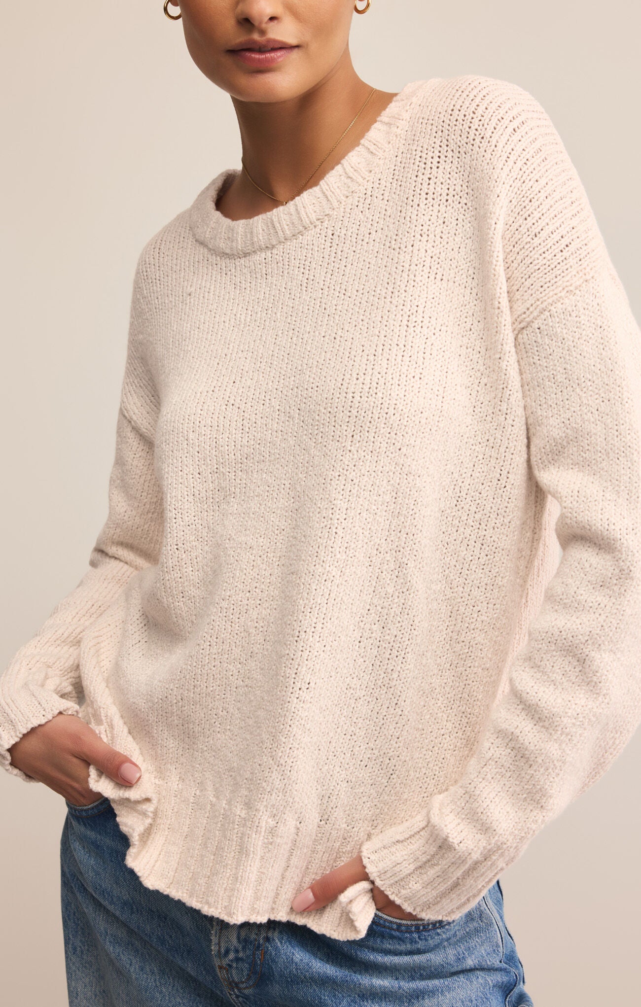Person wearing a light pink sweater and blue jeans against a neutral background