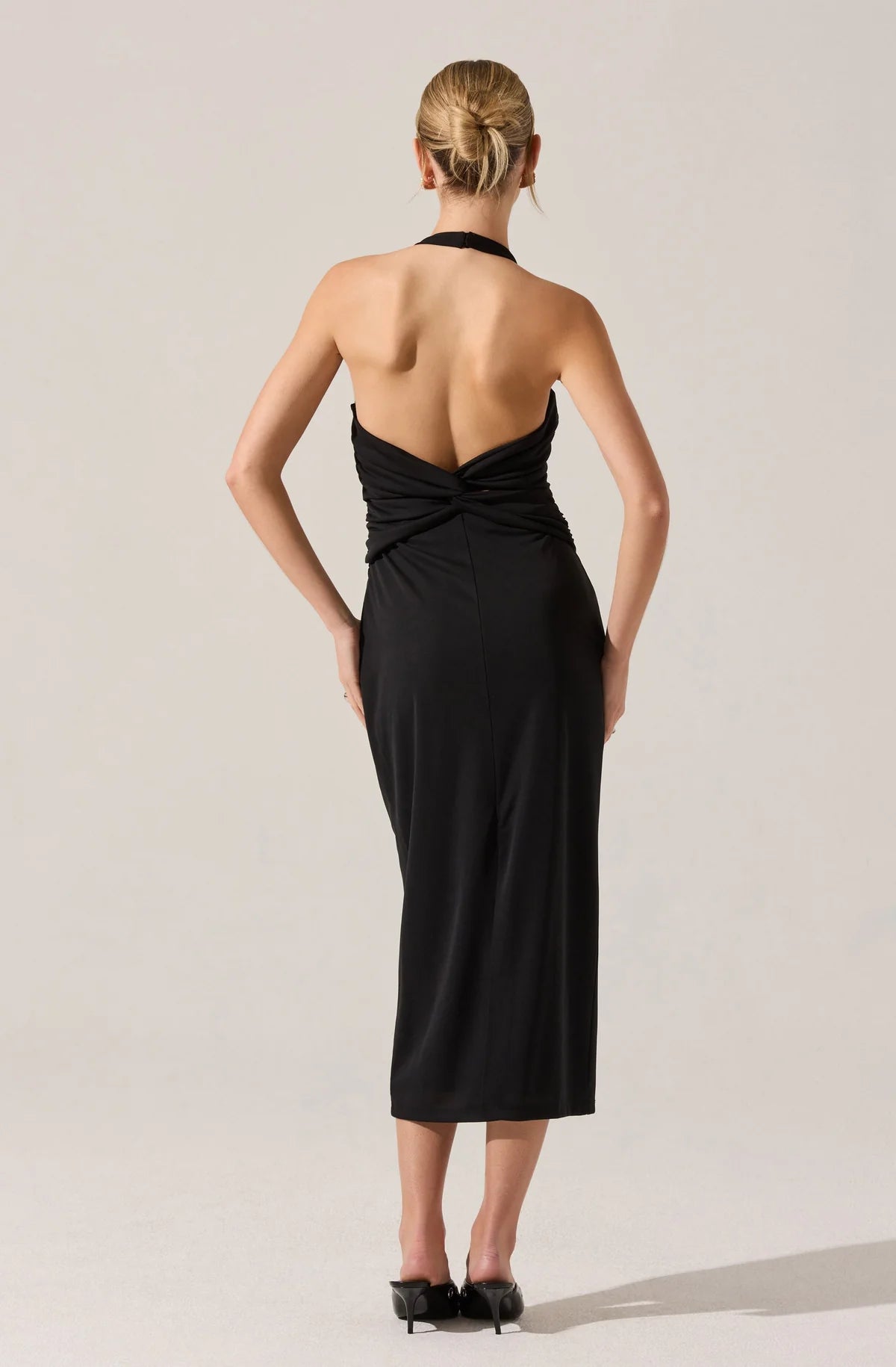 Woman wearing a black halter neck dress with a deep back on a plain background