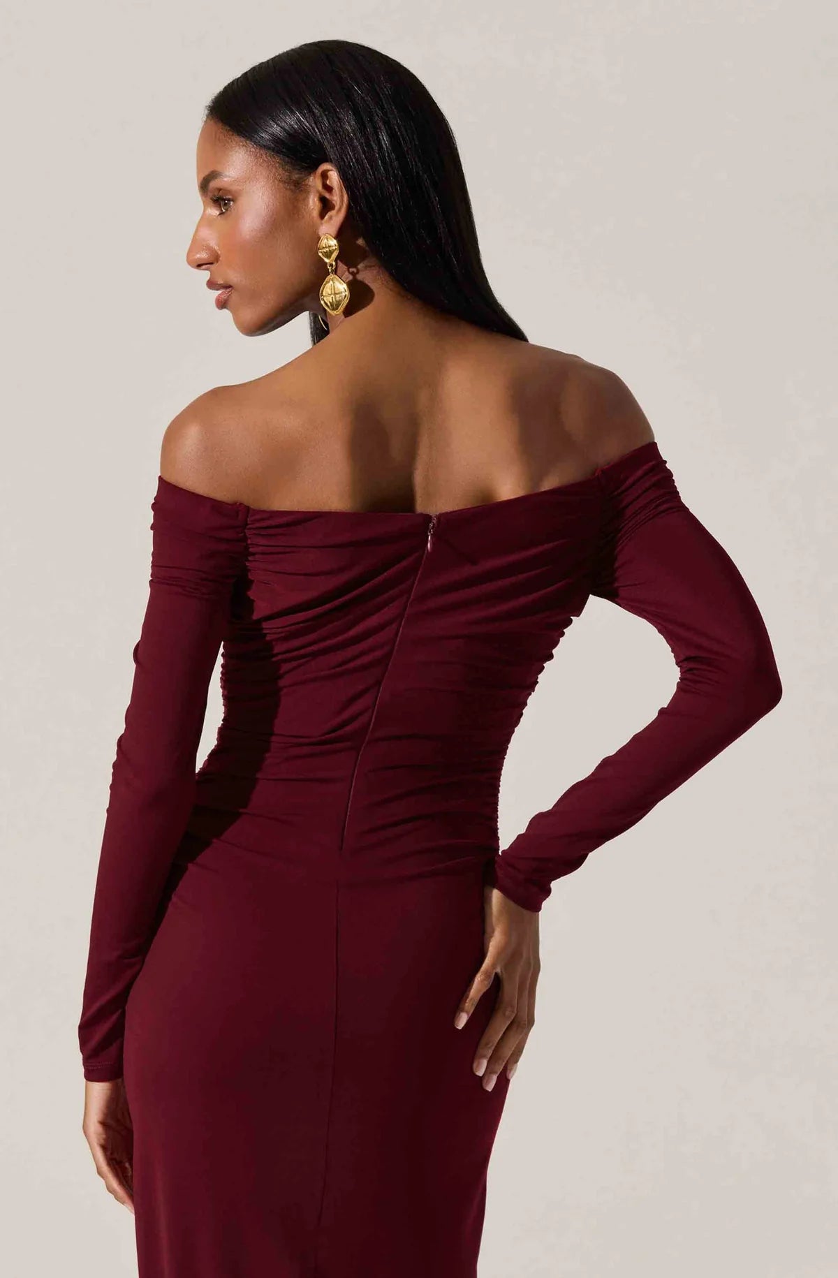 Woman wearing a burgundy off-shoulder dress against a neutral background