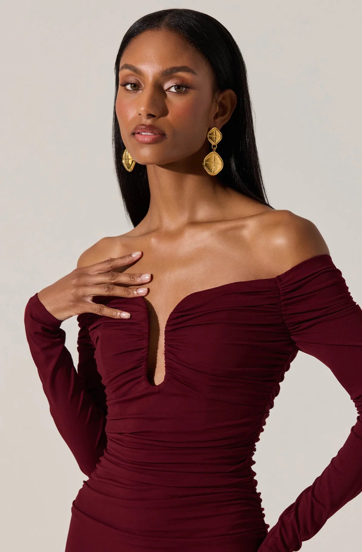Woman wearing a burgundy off-shoulder dress with long sleeves against a neutral background