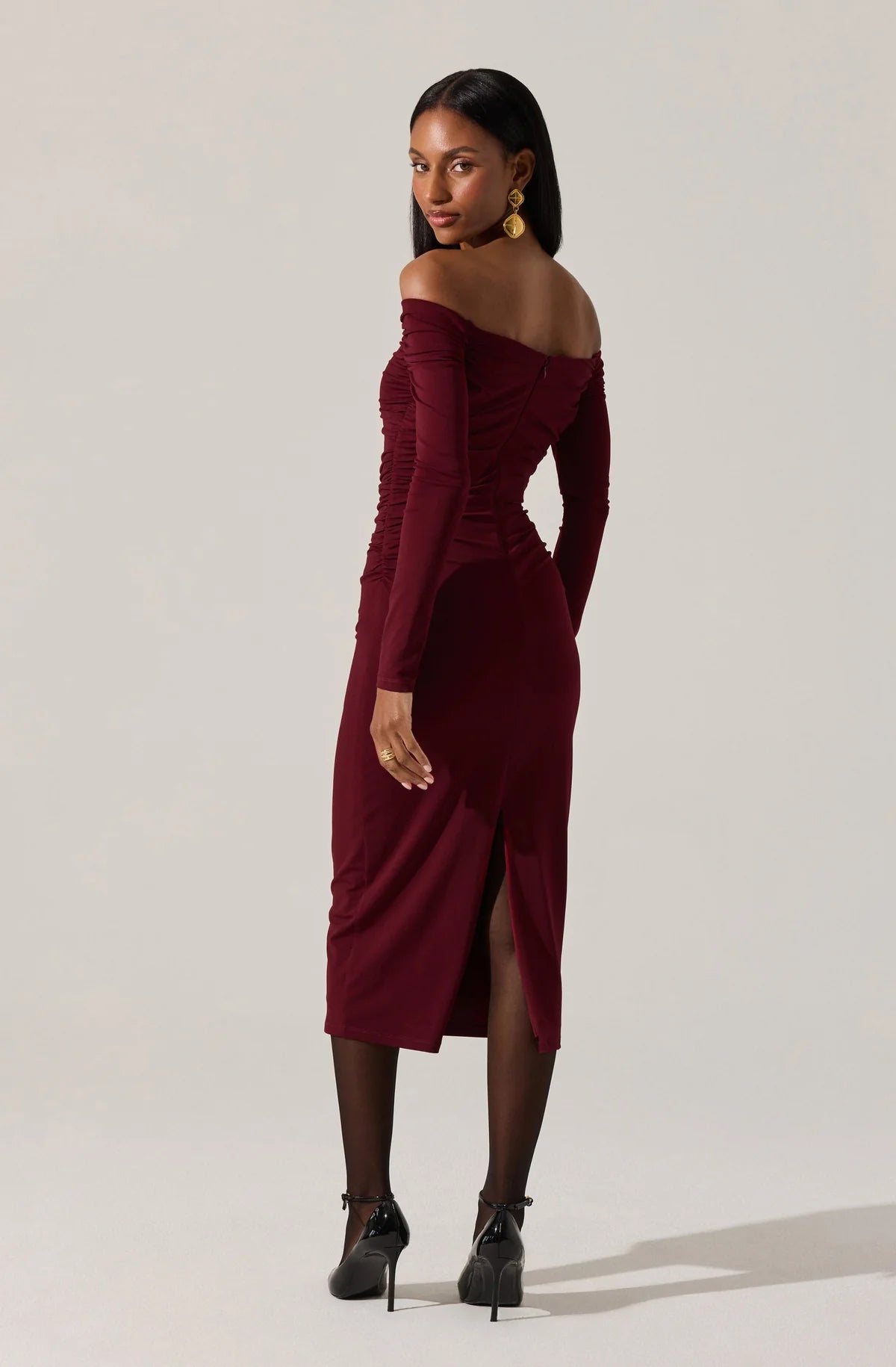 Woman wearing a burgundy off-shoulder dress on a plain background