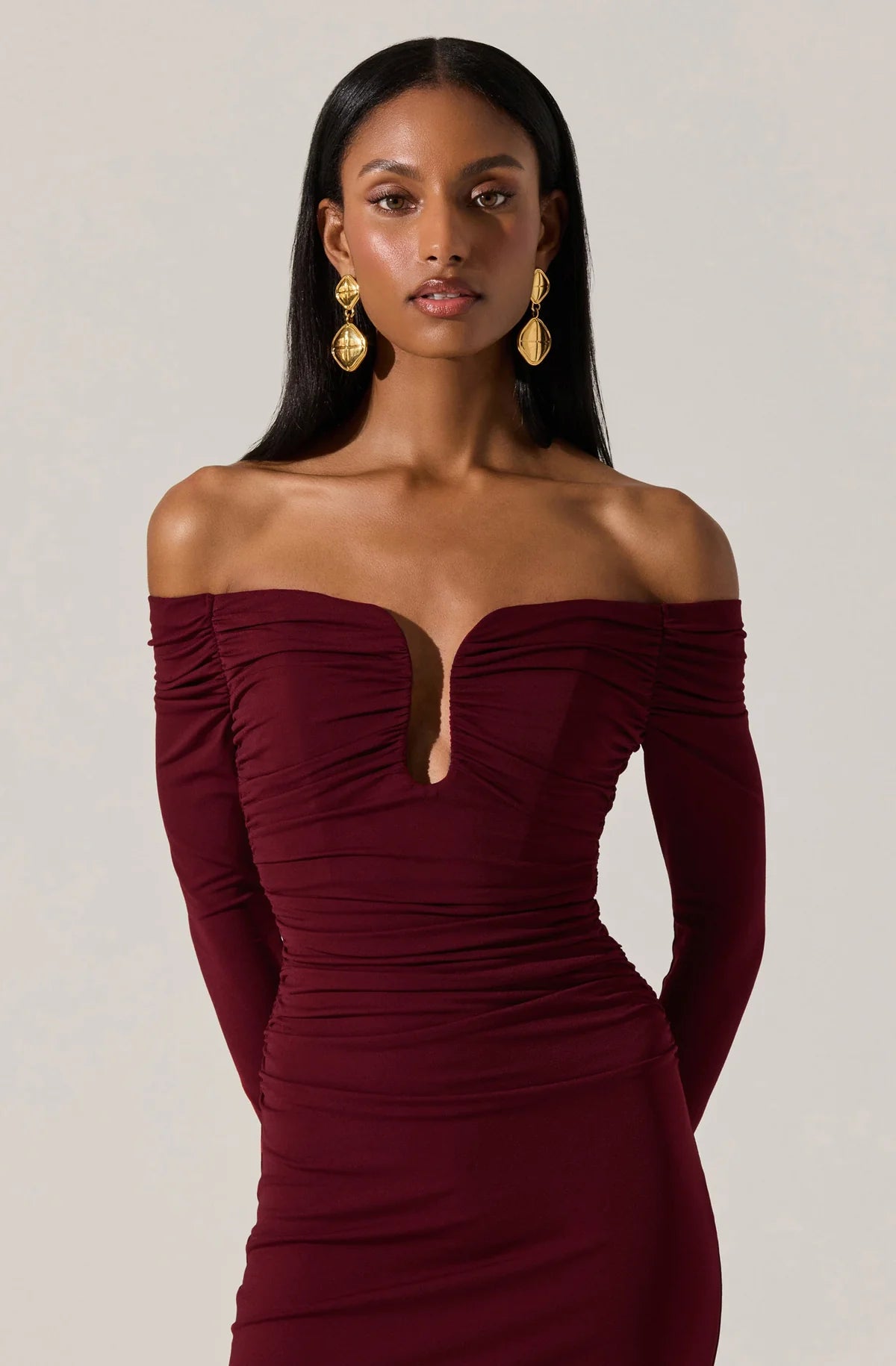 Woman wearing a burgundy off-shoulder dress against a plain background
