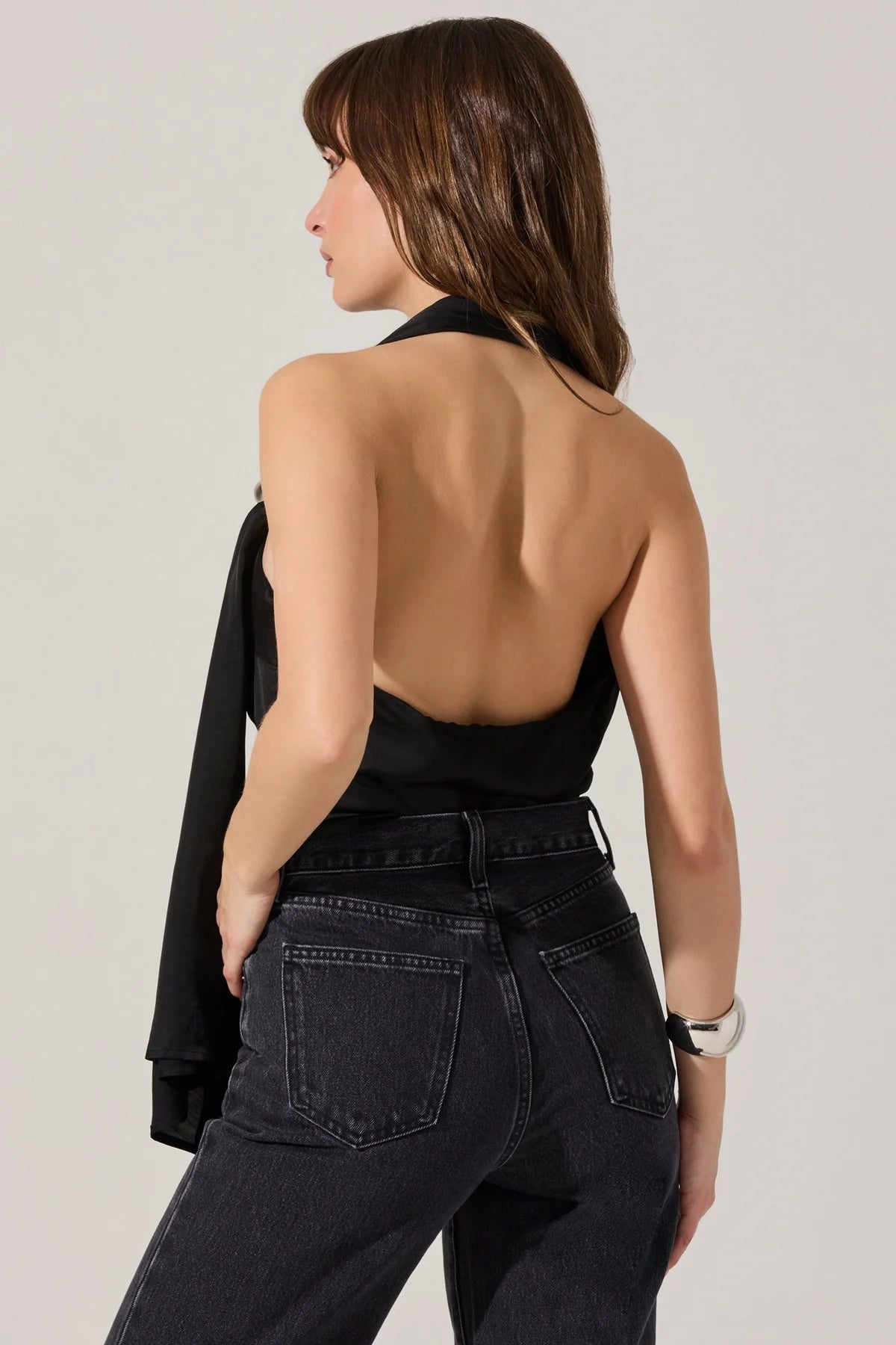Woman wearing a black halter top and high-waisted jeans against a plain background