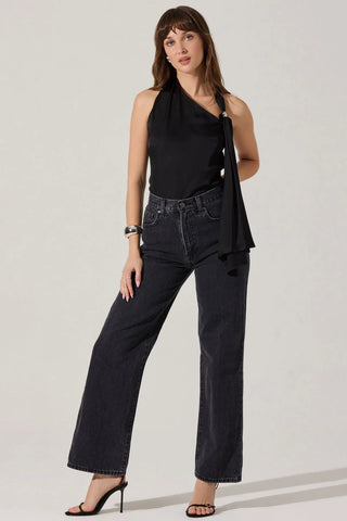 Woman wearing a black halter top and dark jeans on a plain background