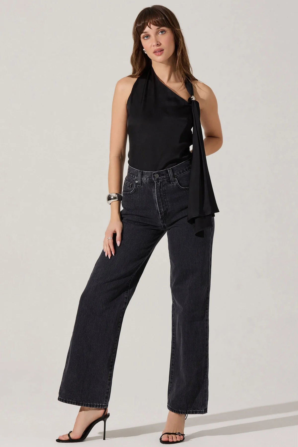 Woman wearing a black halter top and dark jeans on a plain background