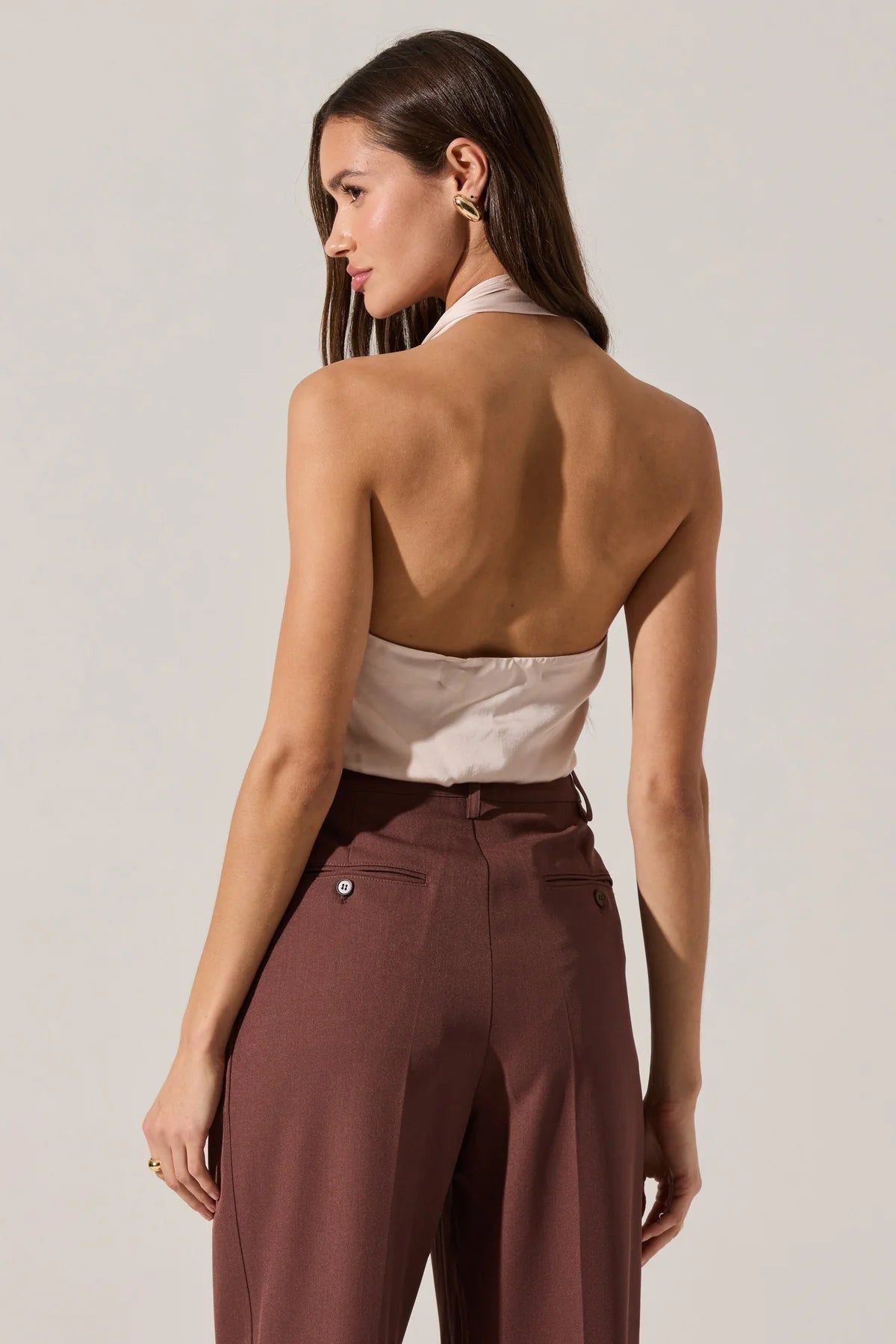 Woman wearing a beige halter top and brown pants against a plain background
